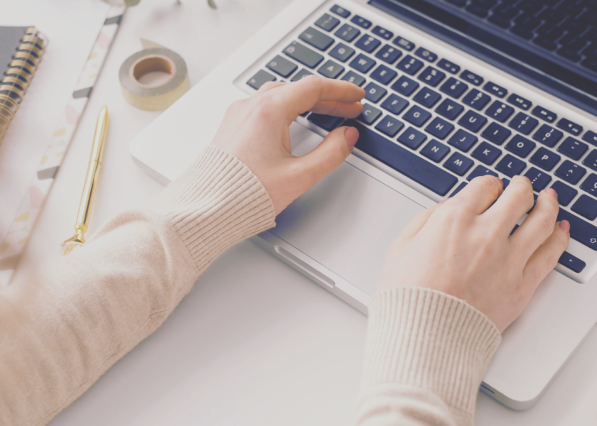 Female medical writer typing on a laptop with a notepad